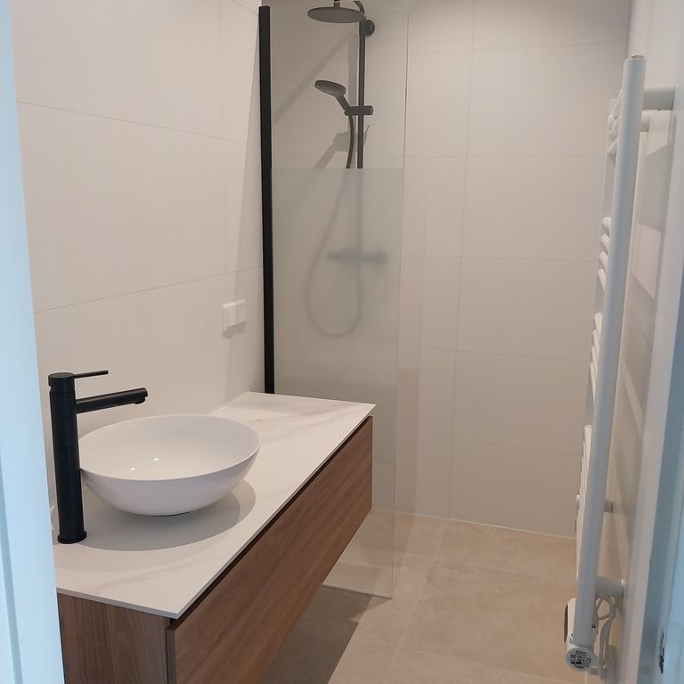 De vernieuwde badkamer met douche en houten meubel